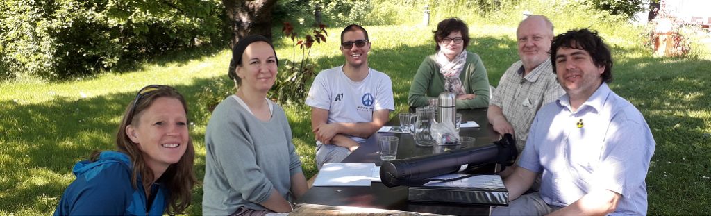 Personen sitzen im Park an einem Tisch und lachen in die Kamera.