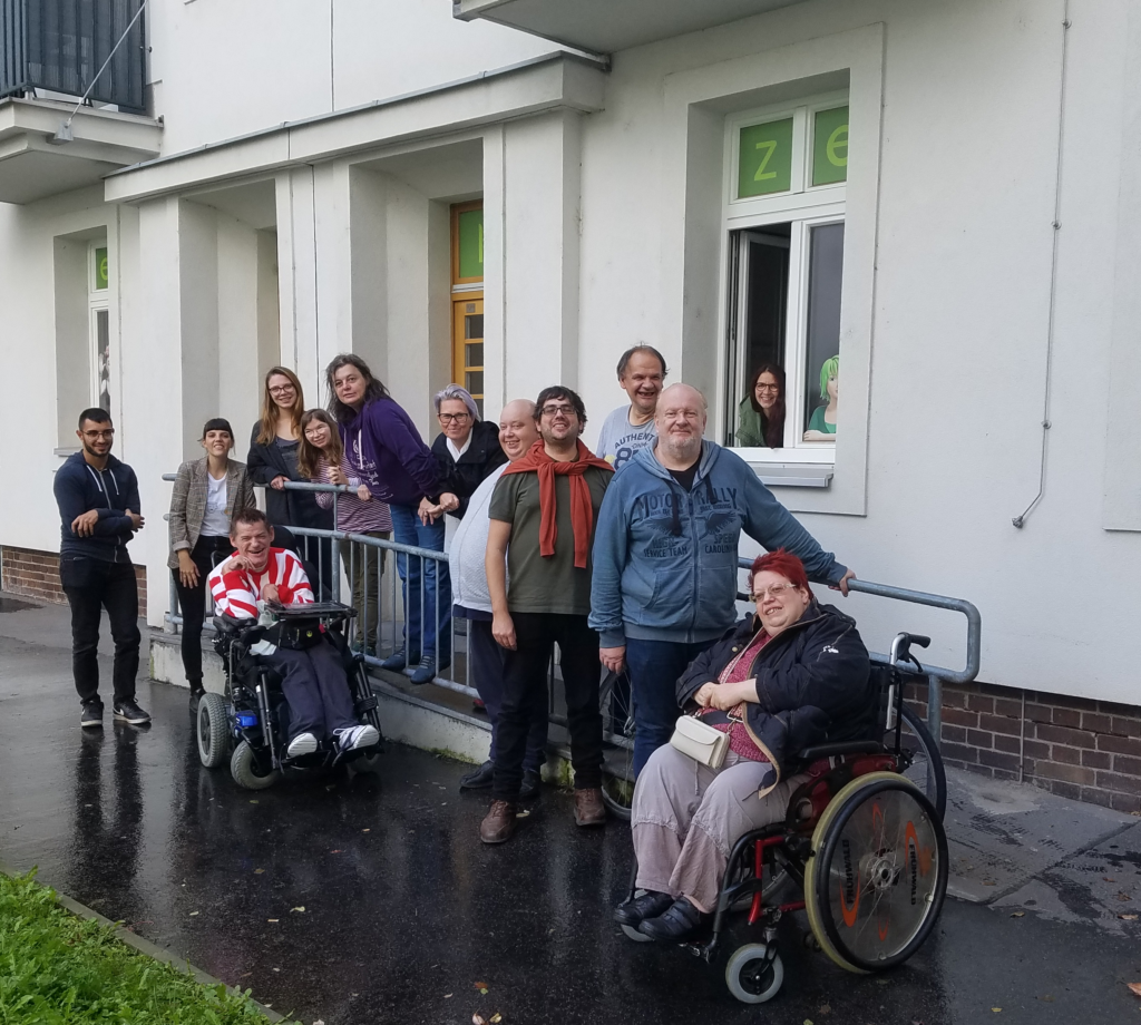 Gruppenfoto von den Mitgliedern der Agentur Sonnenklar und Drehschreibe Peer-Streitschlichtung. Die Personen am Foto stehen bzw. sitzen um die Rampe vor dem Büro.