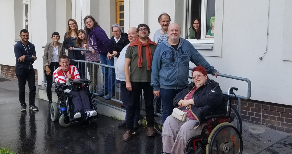 Gruppenfoto von den Mitgliedern der Agentur Sonnenklar und Drehschreibe Peer-Streitschlichtung. Die Personen am Foto stehen bzw. sitzen um die Rampe vor dem Büro.