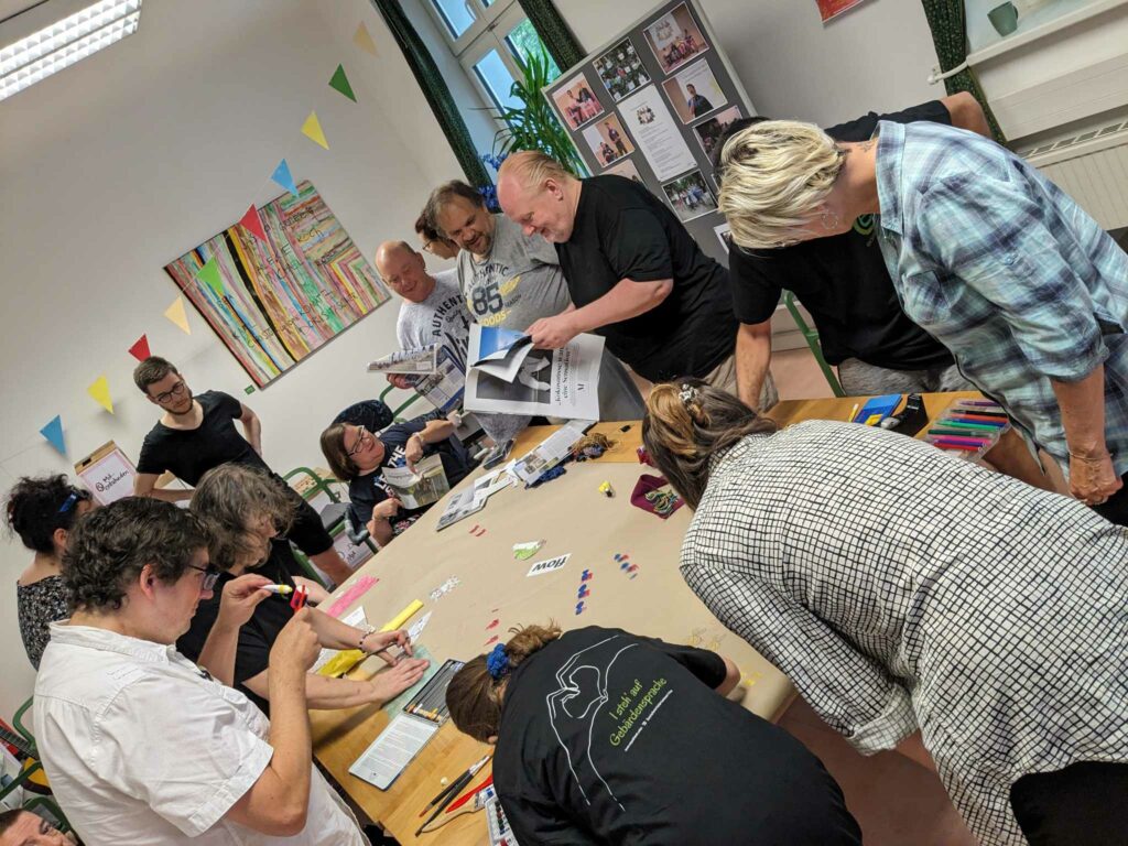 Das Team der Agentur Sonnenklar Drehscheibe Peer Streitschlichtung bei der Klausur. Alle stehen um einen Tisch und bemalen eine Leinwand.