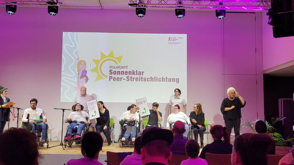 Viele Personen auf einer Bühne beim Theater spielen. Hinter ihnen ist das Logo Sonnenklar Peer-Streitschlichtung projiziert.