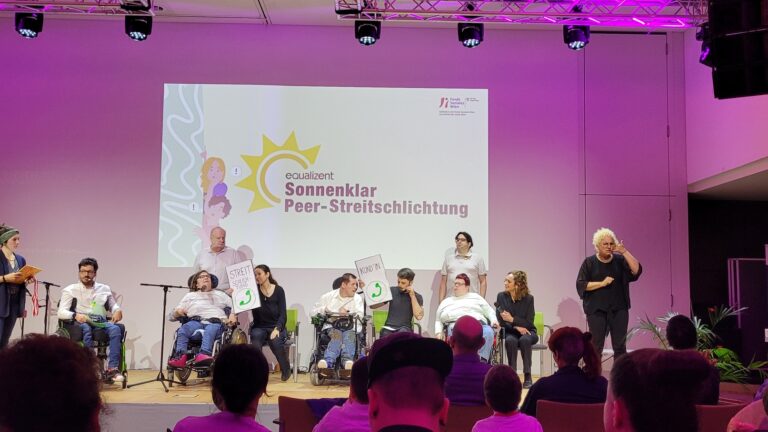 Viele Personen auf einer Bühne beim Theater spielen. Hinter ihnen ist das Logo Sonnenklar Peer-Streitschlichtung projiziert.