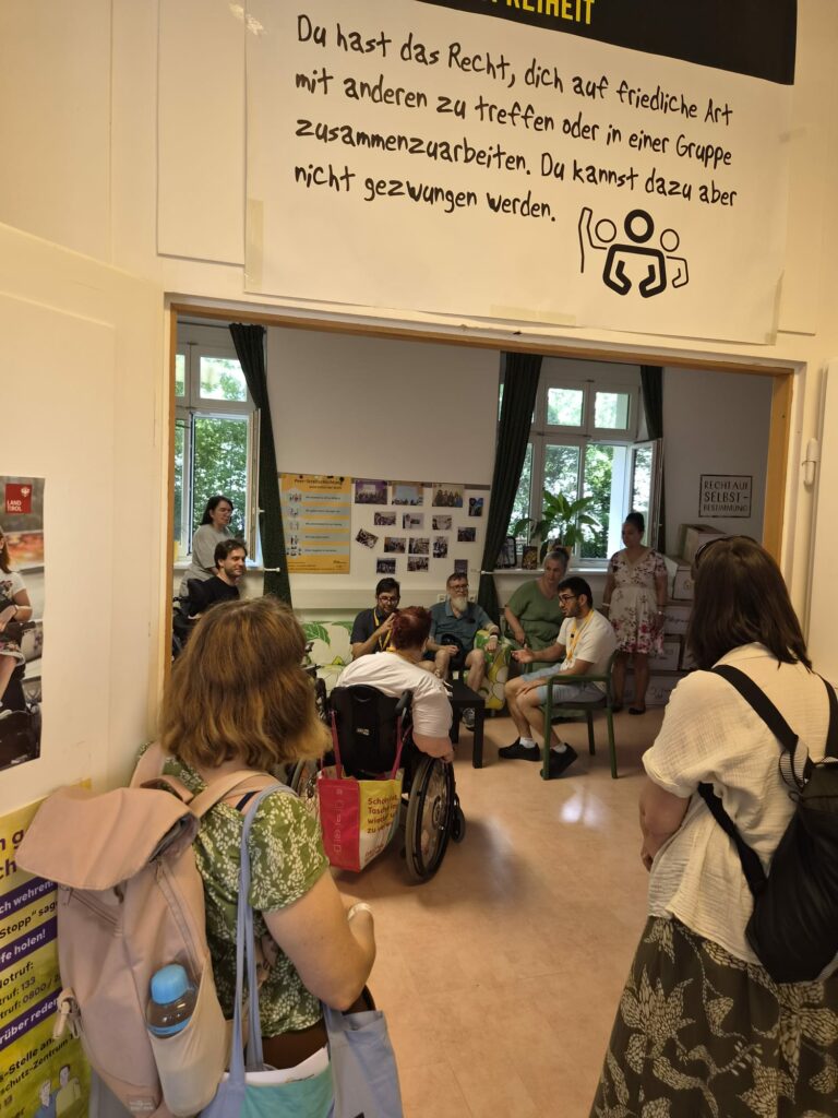 Aufnahme von mehreren Personen während eines Rollenspiels am Infotag. In der Mitte sitzen die Streitschlichter*innen die Schauspielern. Rundherum sitzen oder stehen Zuseher*innen.